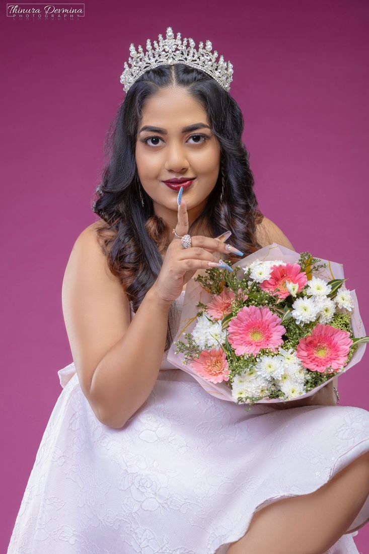 Crowned birthday portrait with a finger to her lips and a bouquet of gerberas