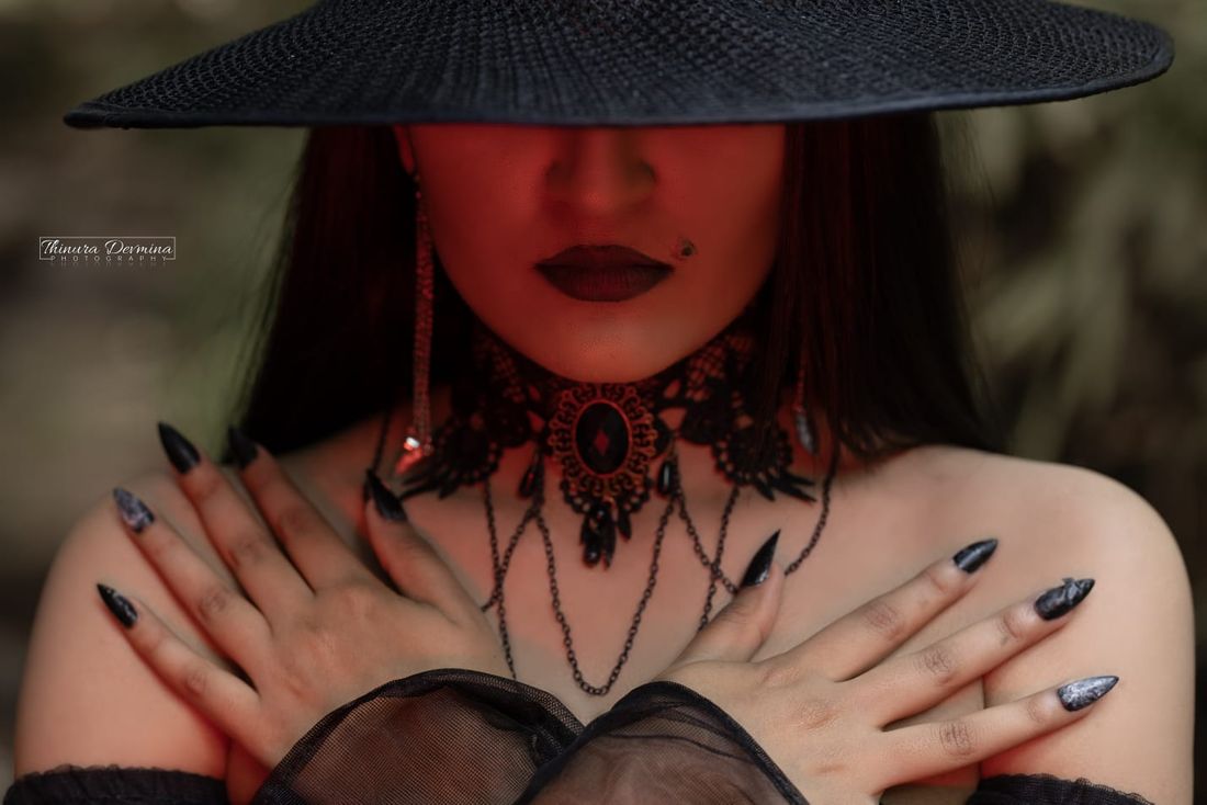 Hands crossed over a lace choker beneath a wide-brim hat