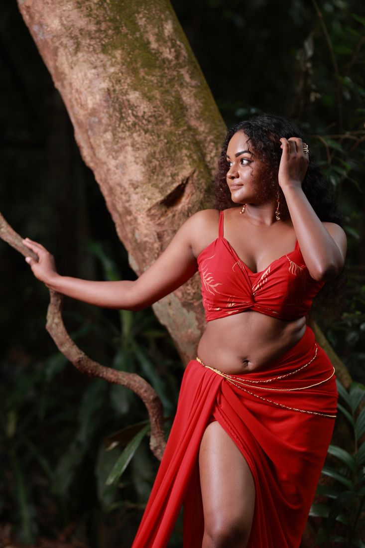 Model in a red draped outfit posing against a tree