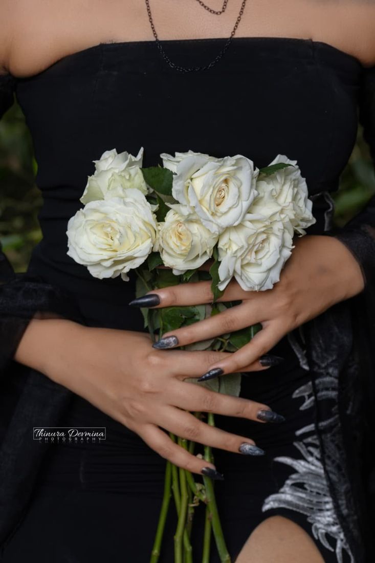 Hands with black nails holding white roses